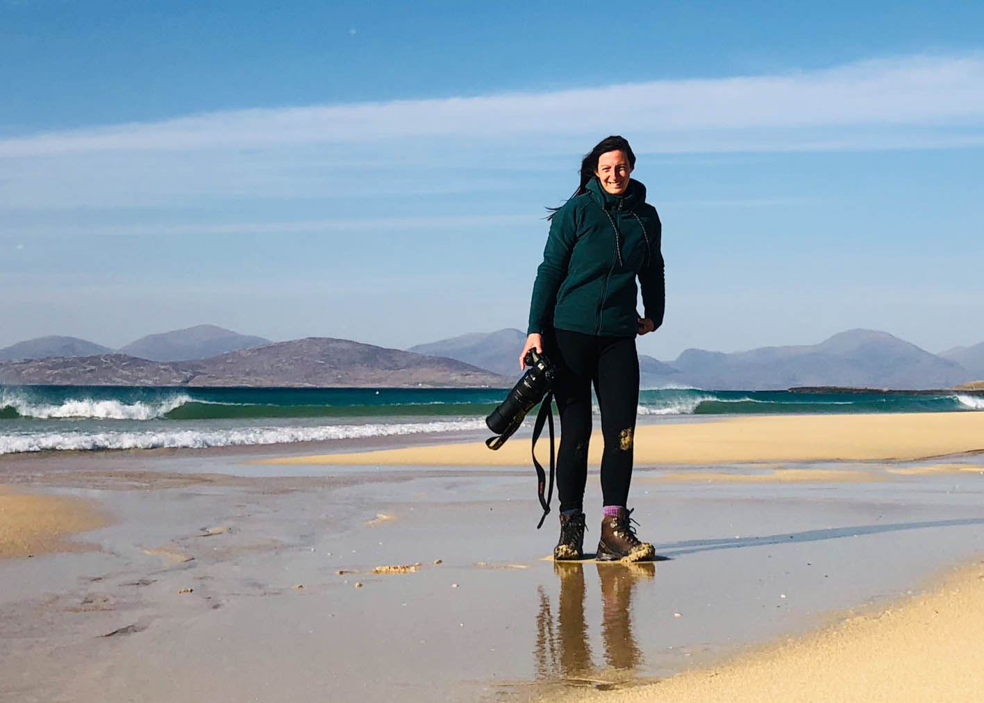 Isle of Harris photographer Margaret Soraya holding a camera and standing on the beach. Margaret offers one to one tuition and creative mentoring.